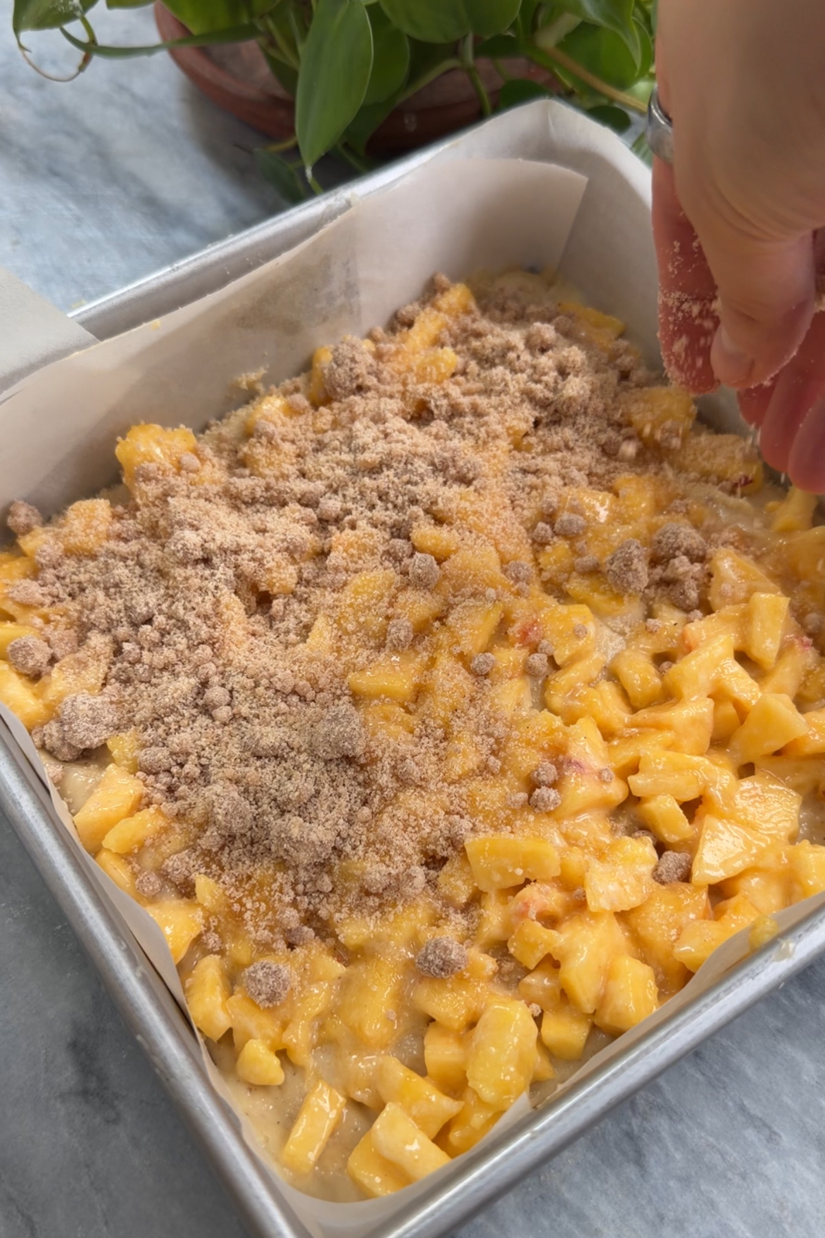 Brown butter peach coffee cake being layered with batter, streusel, and chopped peaches before baking.