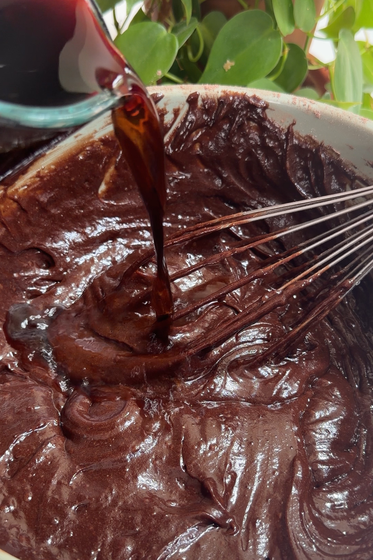 Hot coffee being poured into chocolate batter in a green mixing bowl for a dark chocolate raspberry layer cake.