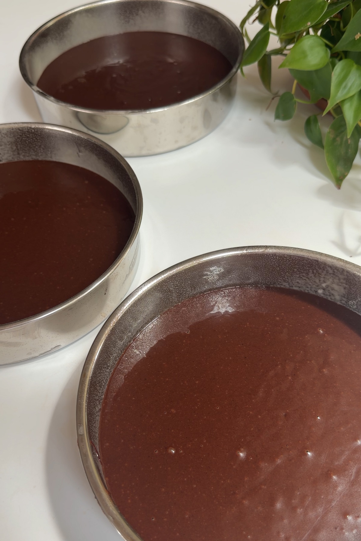 Three prepped 8-inch cake pans filled with chocolate batter for a dark chocolate raspberry layer cake.