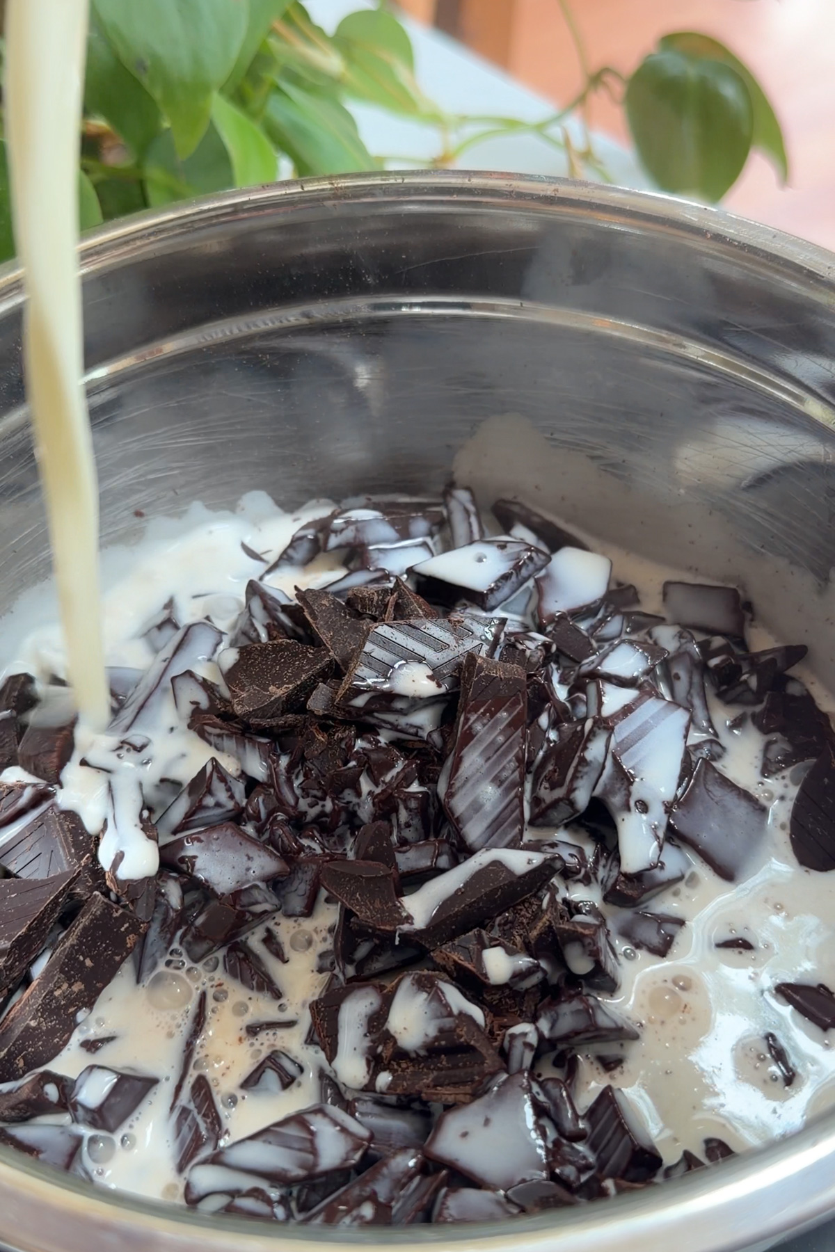 Warm heavy cream pouring onto chopped dark chocolate to make chocolate ganache frosting for a dark chocolate raspberry layer cake.