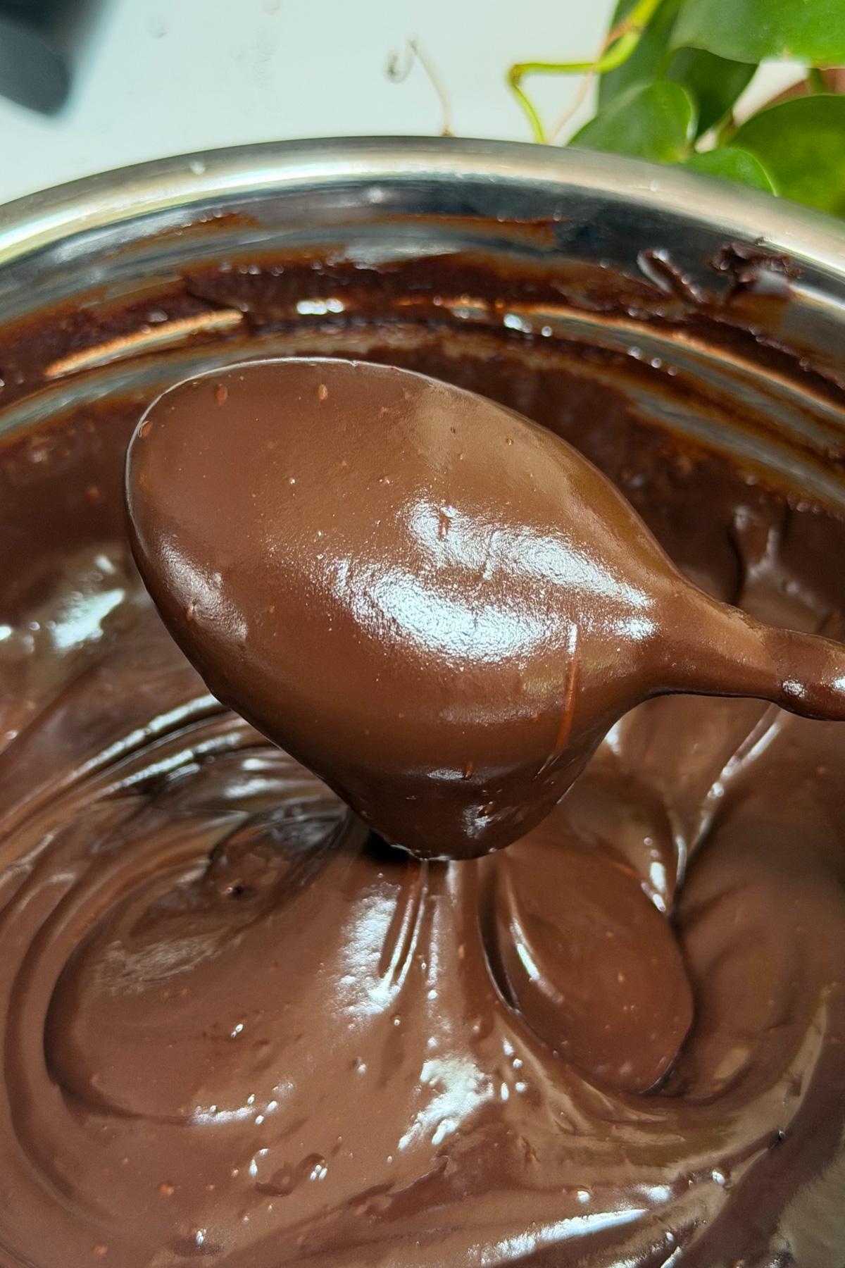 Dark chocolate ganache frosting on a spoon to show its smooth texture before being added to a dark chocolate raspberry layer cake.