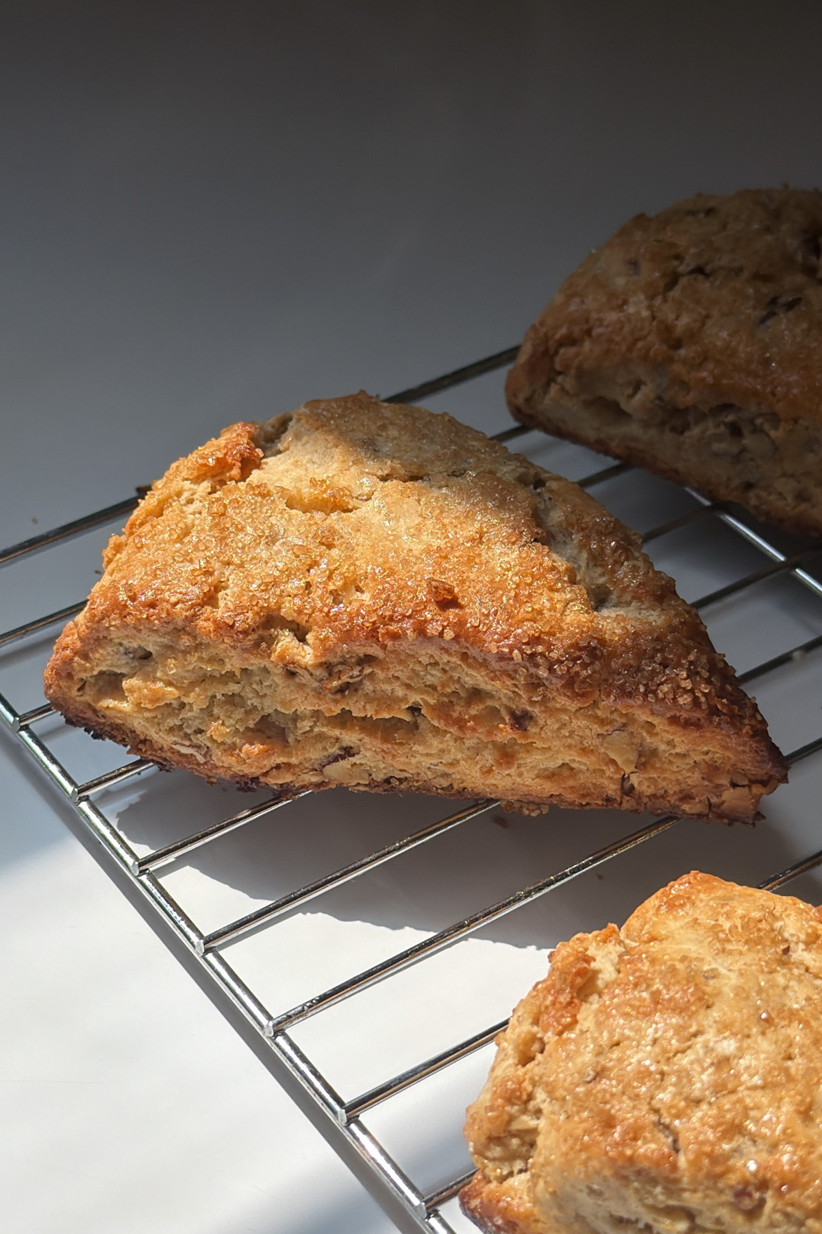 A maple pecan scone topped with turbinado sugar on a cooling rack after baking.