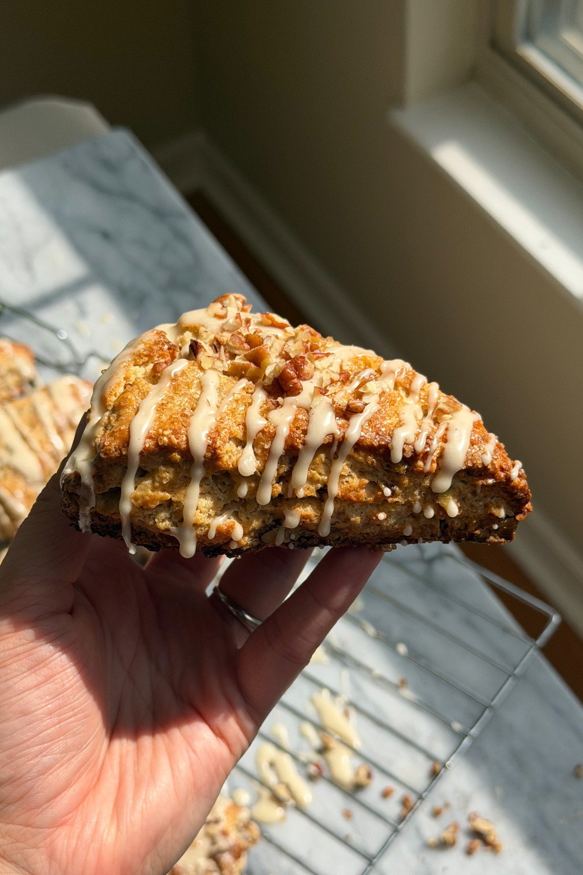 A hand holding a maple pecan scone covered in maple glaze and topped with chopped pecans.