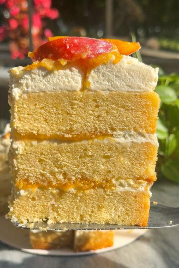 Brown butter bourbon peaches and cream layer cake slice in front of the rest of the cake.