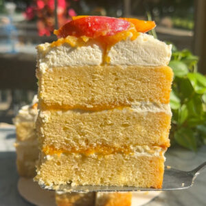 Brown butter bourbon peaches and cream layer cake slice in front of the rest of the cake.