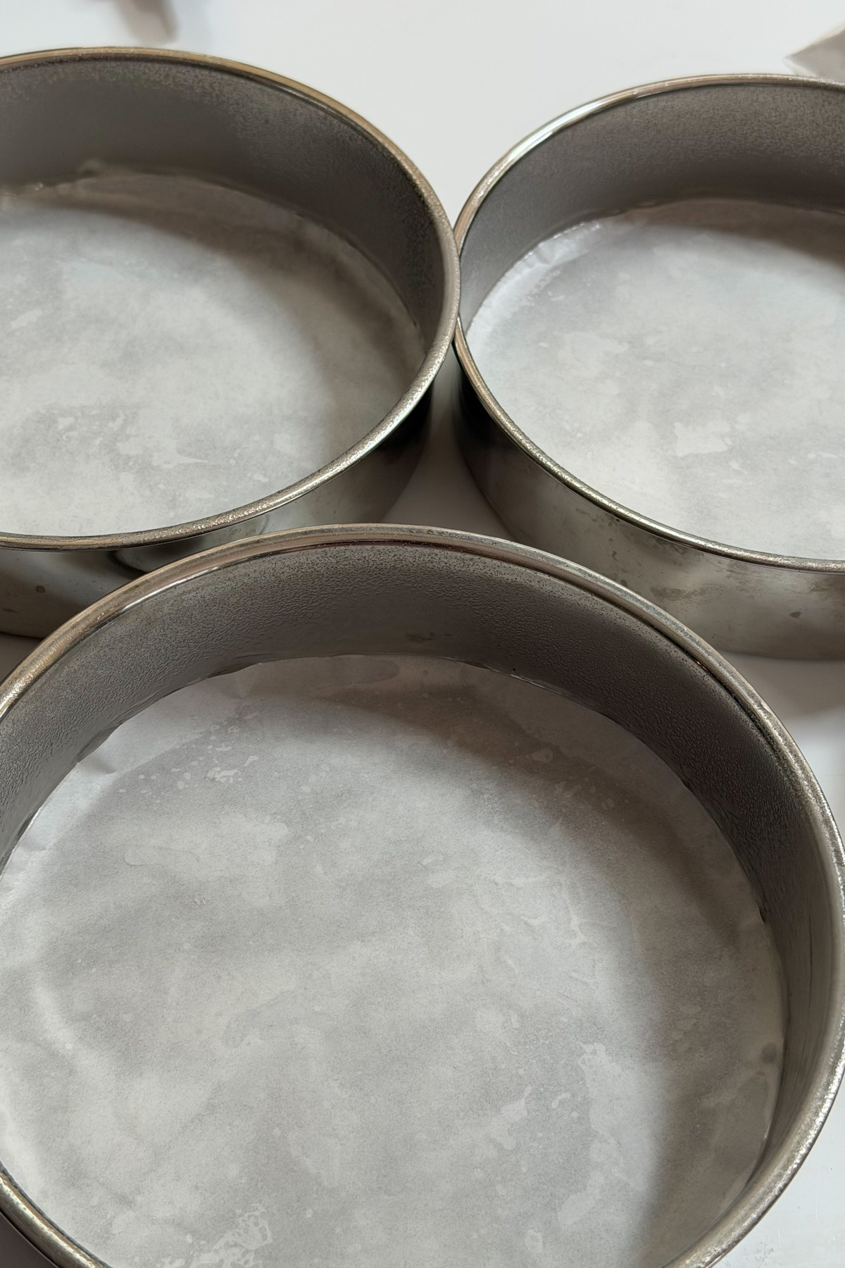 Three prepped 8-inch round cake pans for peaches and cream cake.