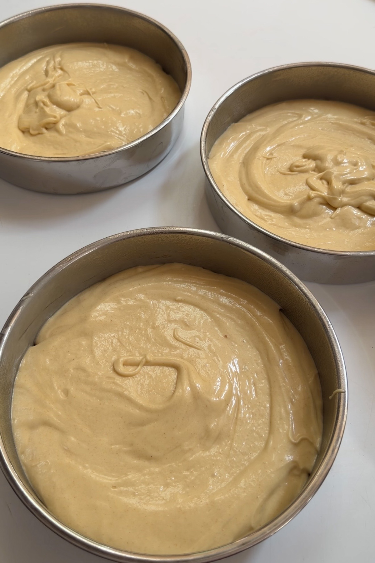 Brown butter cake batter in three 8-inch round cake pans for brown butter bourbon peaches and cream cake before baking.