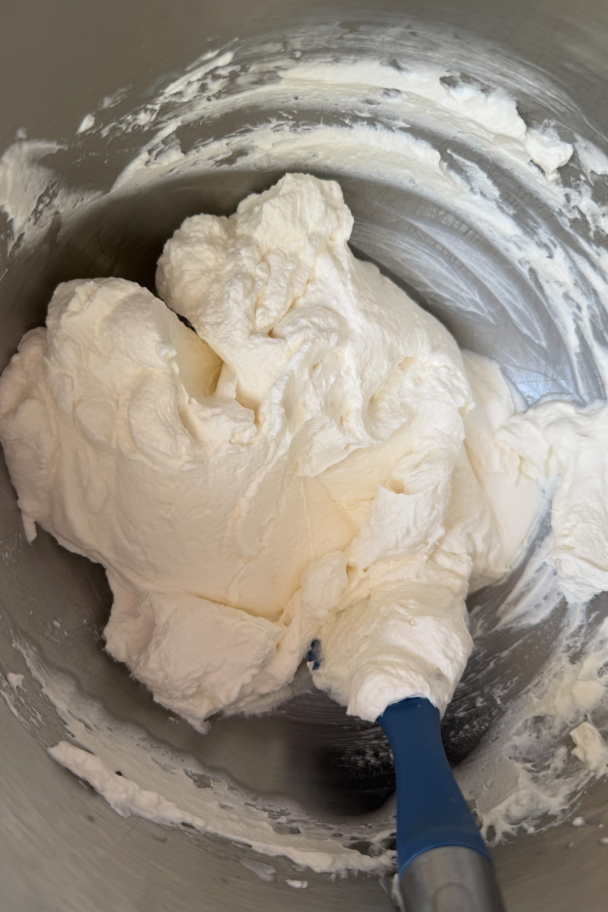 Whipped cream frosting in a stainless steel mixing bowl for brown butter bourbon peaches and cream cake.