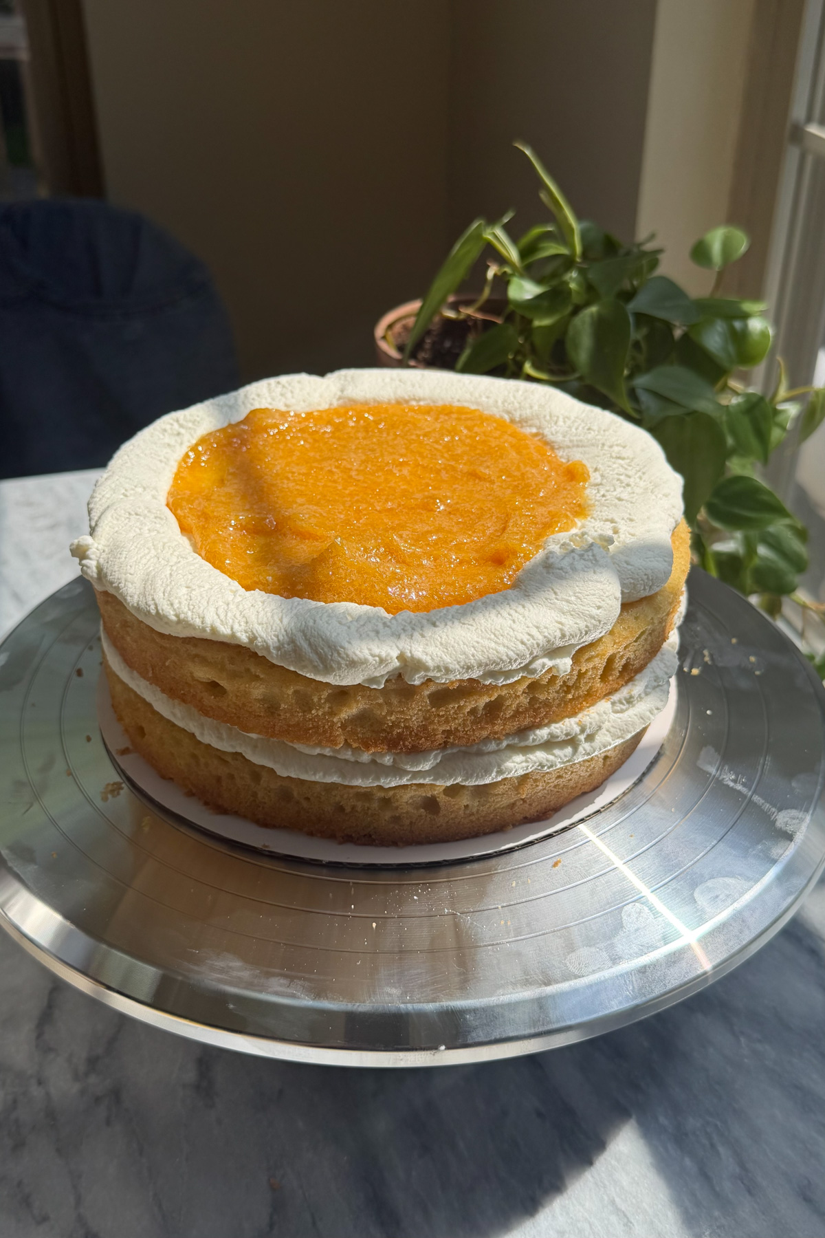 A brown butter bourbon peaches and cream cake being assembled with peach compote in the middle.