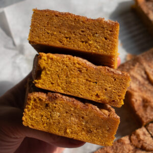 A hand holding three pumpkin blondies stacked on top of each other.