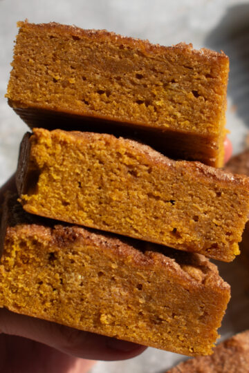 A hand holding three pumpkin blondies stacked on top of each other.