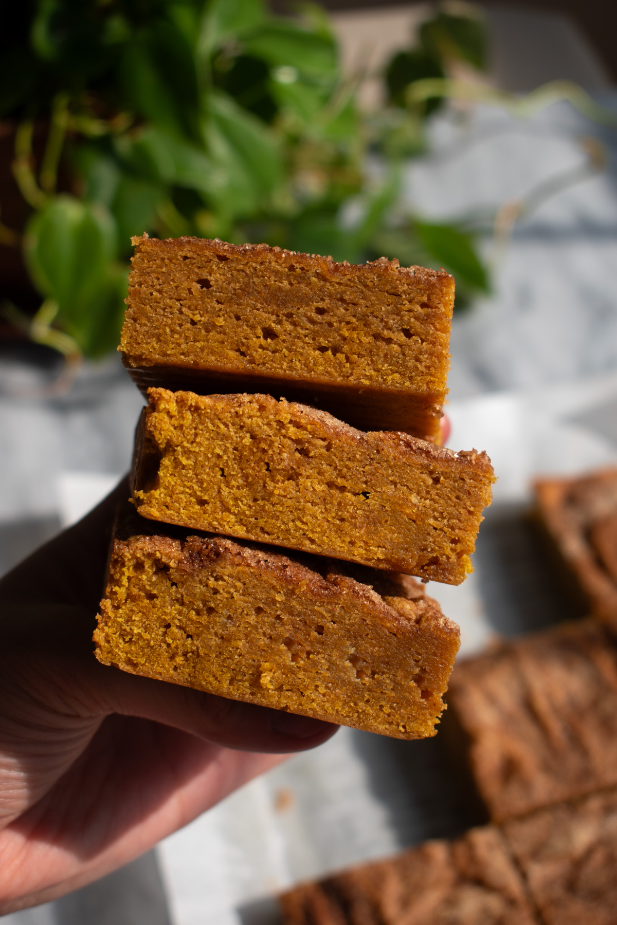 A hand holding three pumpkin blondies stacked on top of each other.
