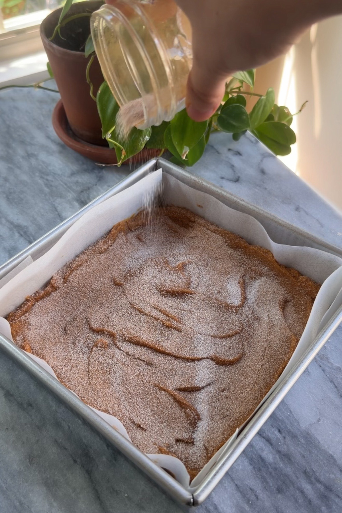 The batter for cinnamon sugar pumpkin blondies in a lined 8x8 baking pan, topped with cinnamon sugar before being baked.