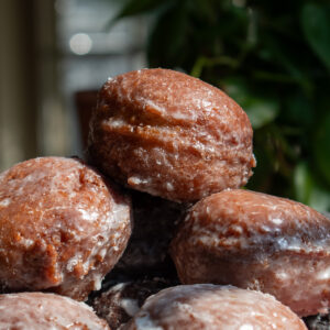 Glazed applesauce fritters stacked on top of each other to show their shiny, cracked texture.