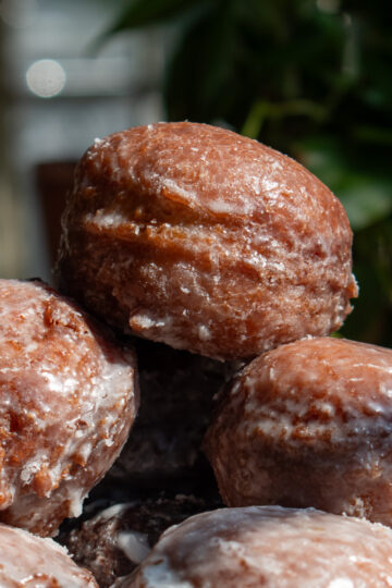 Glazed applesauce fritters stacked on top of each other to show their shiny, cracked texture.