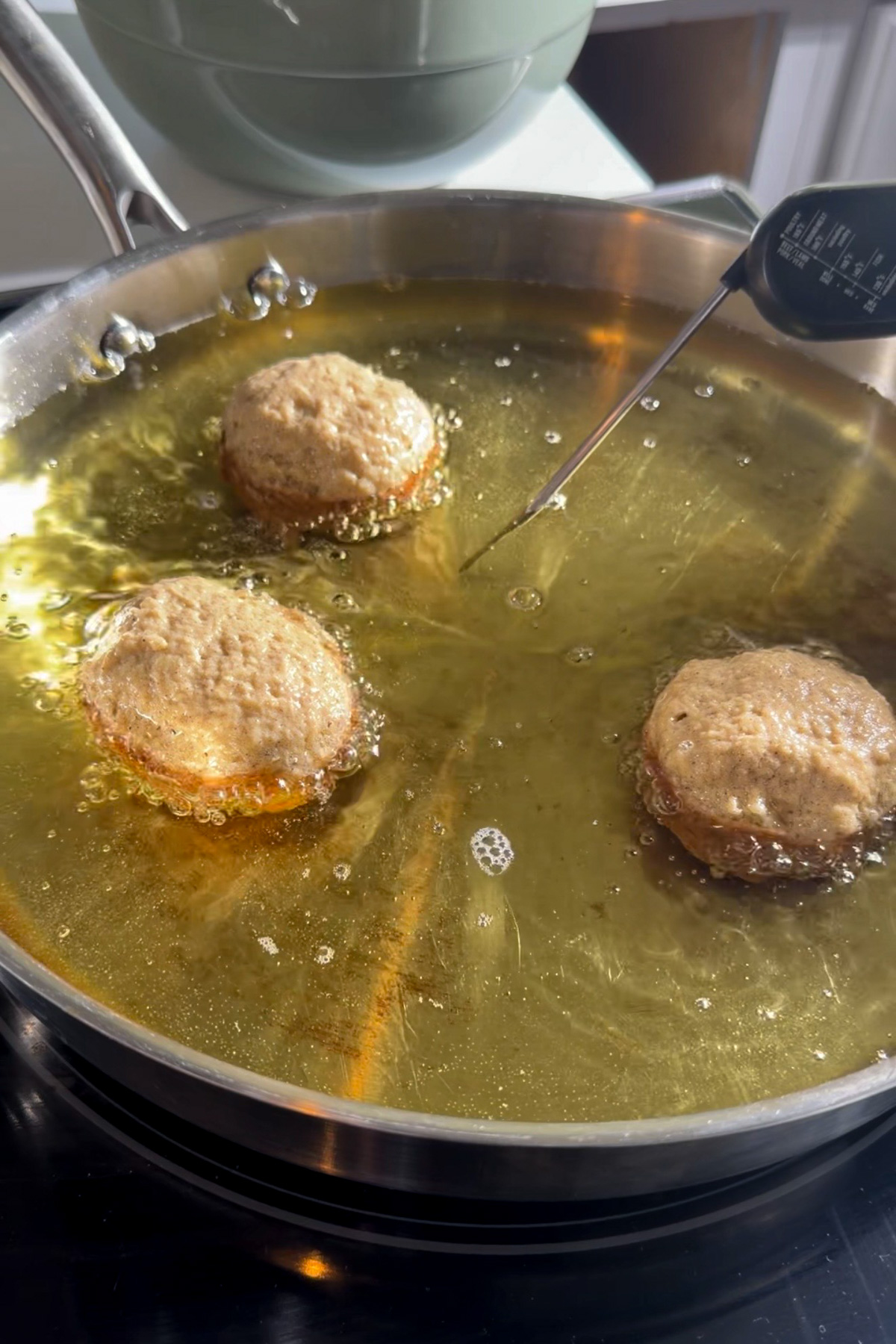 Applesauce fritter batter frying in hot oil in a stainless steel pan.