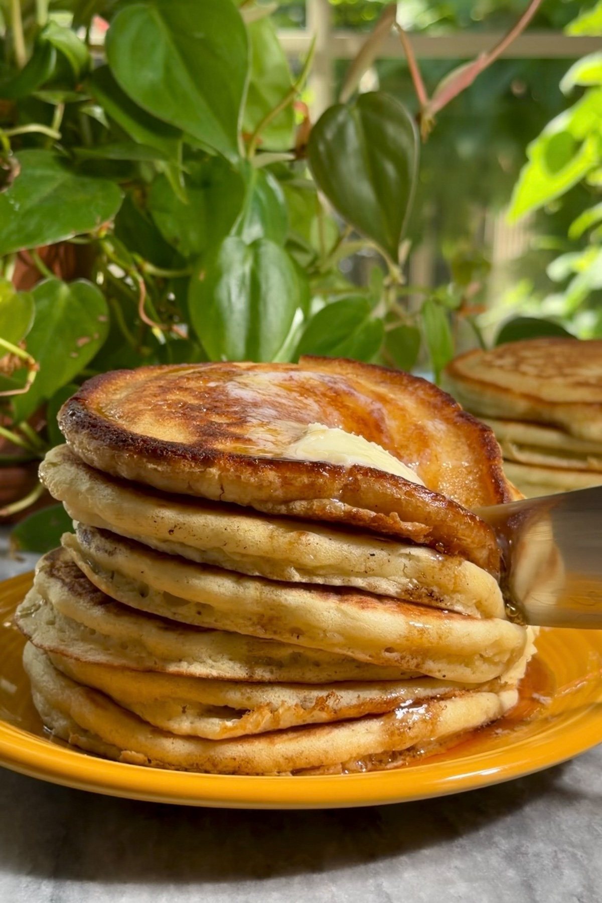 Six fluffy sourdough discard pancakes stacked on a yellow plate being sliced with a knife.