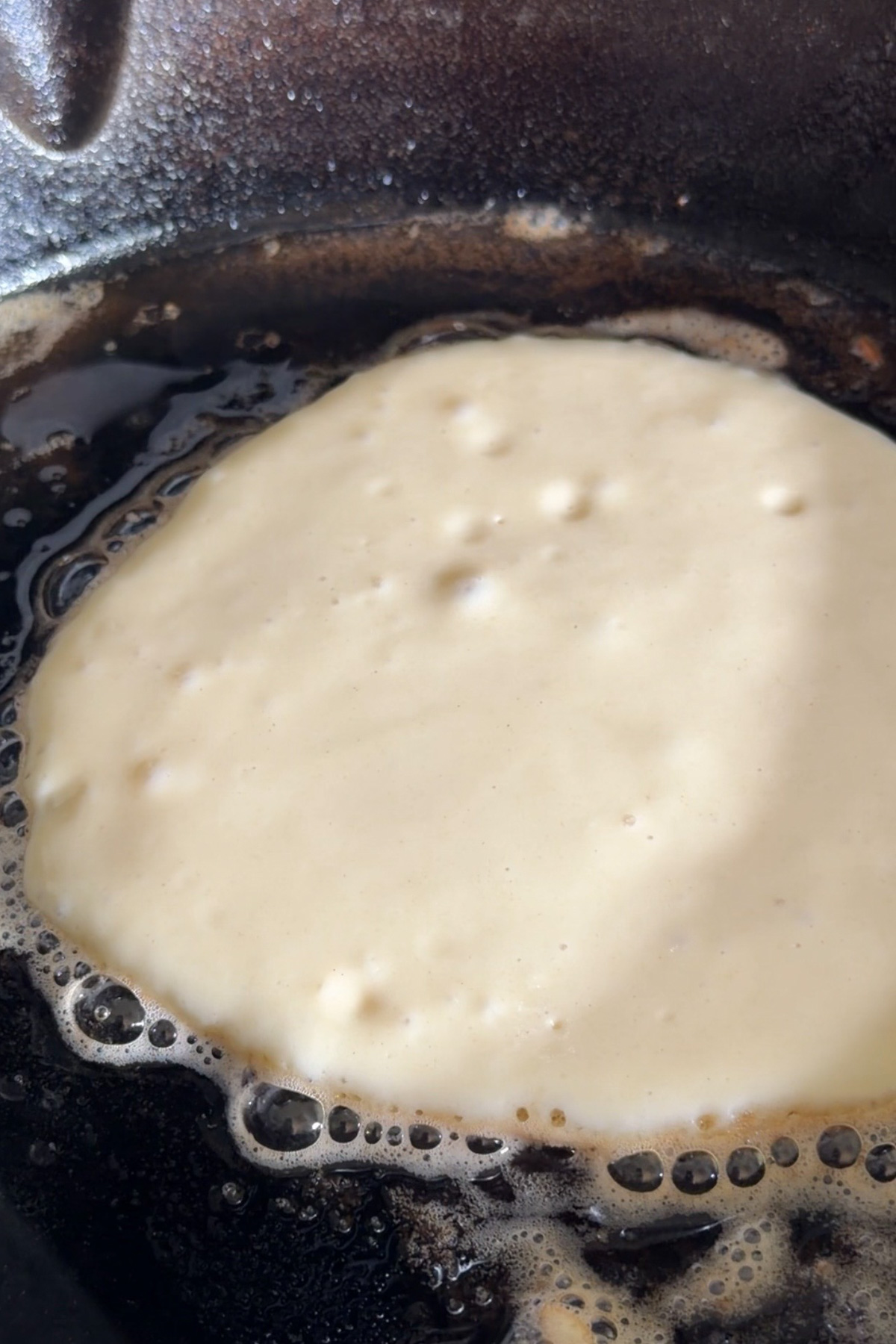 Fluffy sourdough discard pancake batter in a hot cast iron skillet before flipping.