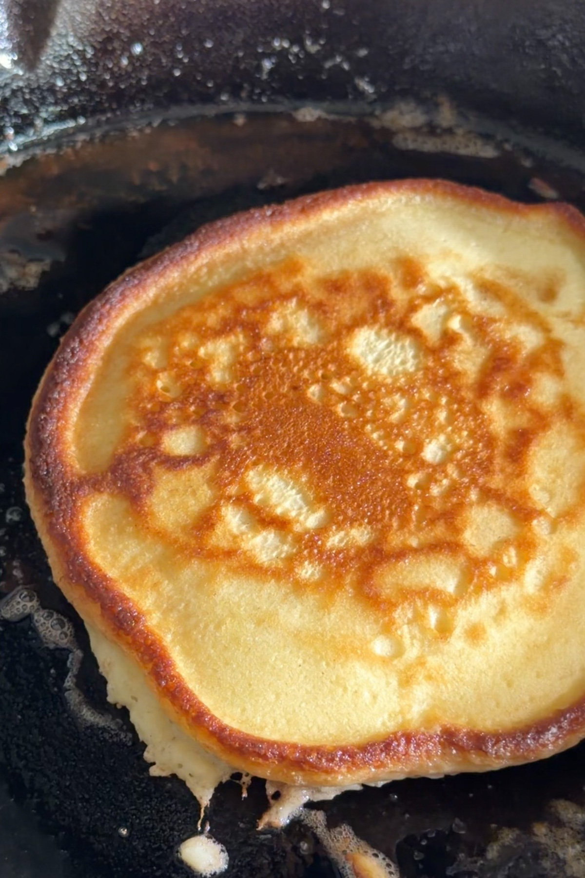 Fluffy sourdough discard pancake batter in a hot cast iron skillet before and after flipping to show the golden buttery texture.