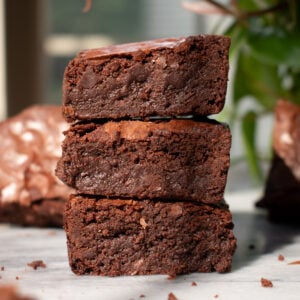 Three crackly fudgy brownies stacked on top of each other on a marble countertop.