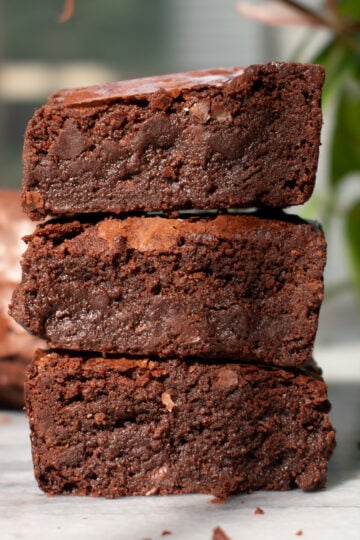 Three crackly fudgy brownies stacked on top of each other on a marble countertop.