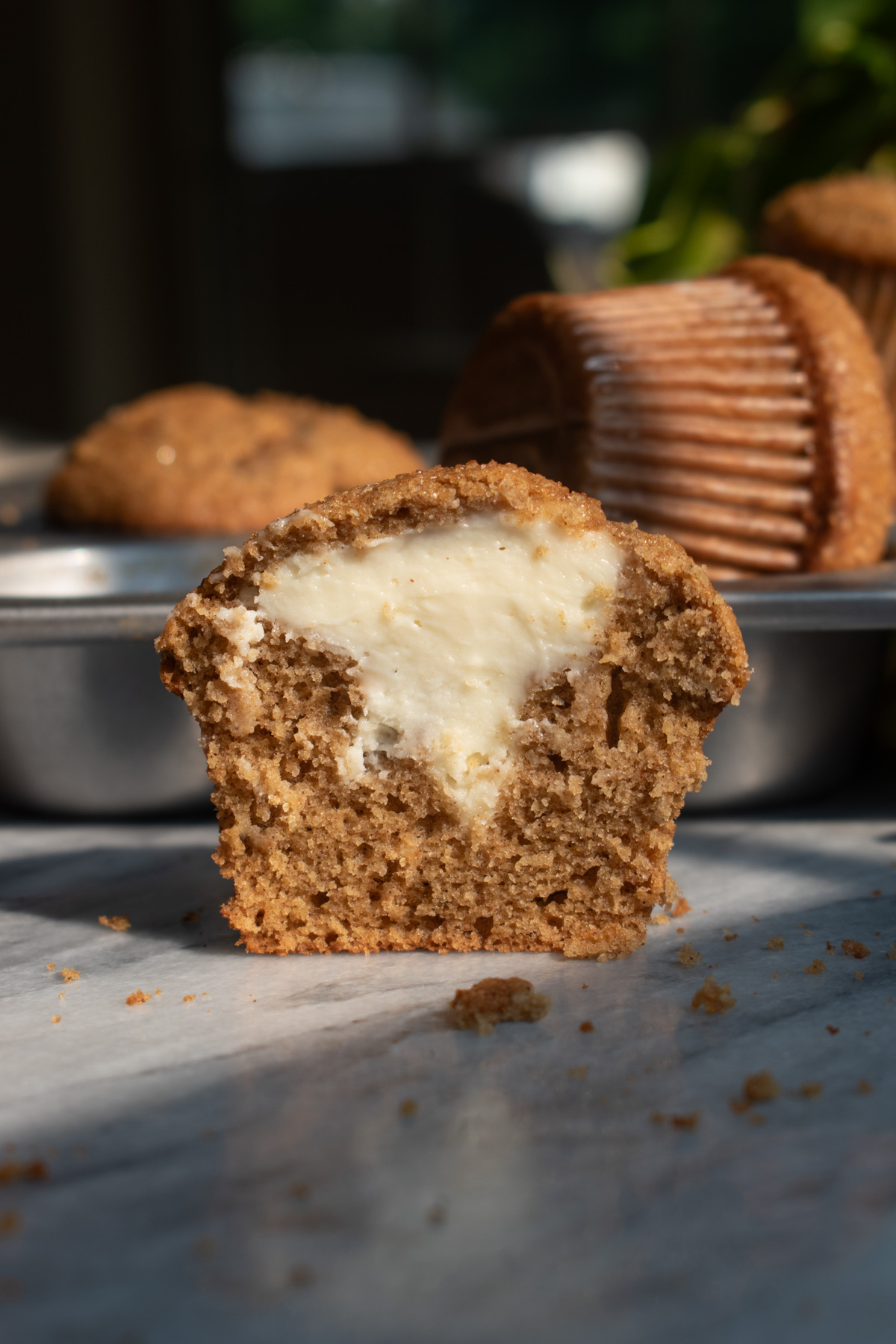 Half of a cheesecake-stuffed apple butter muffin sitting on a marble countertop to show the layers with a window and more muffins in the background.