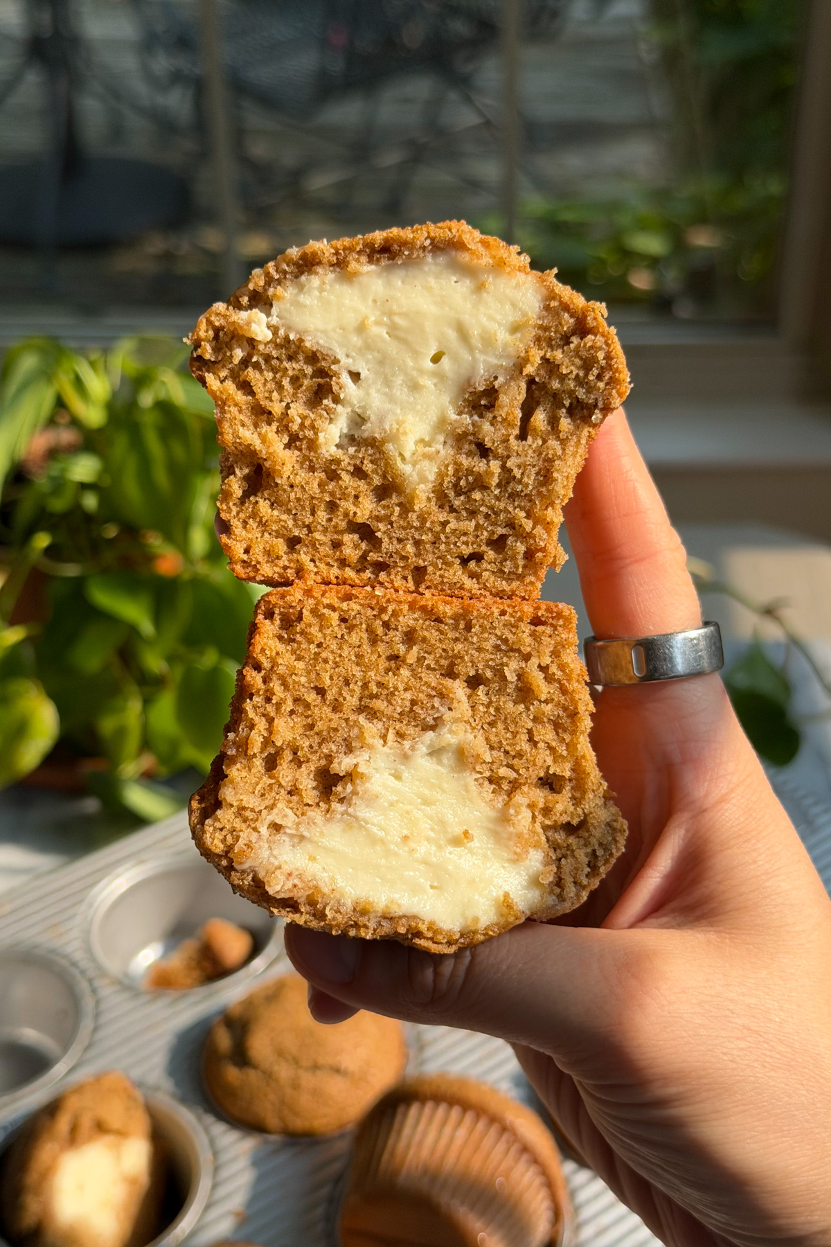A hand holding two halves of a cheesecake-stuffed apple butter muffin, stacked on top of each other to show the soft texture and symmetrical cheesecake filling.