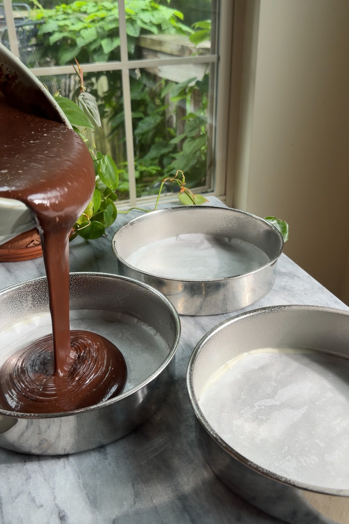 The chocolate cake batter for Matilda's Chocolate Cake being poured into 3, 8-inch cake rounds.