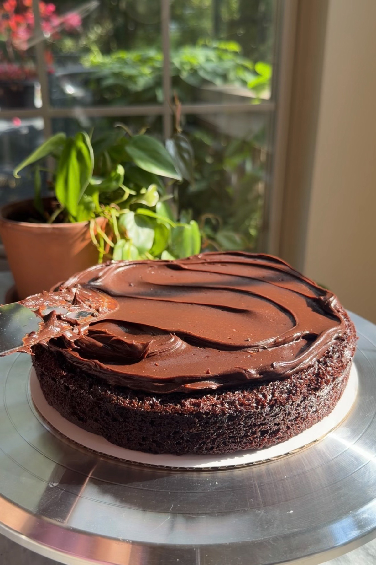 The first layer of Matilda's Chocolate Cake being covered in a smooth, shiny chocolate ganache frosting.