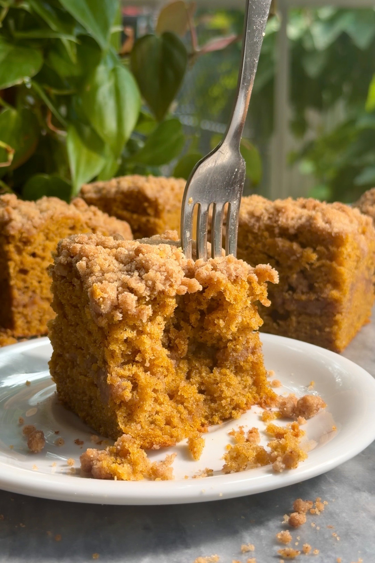 A fork cutting into a slice of moist pumpkin coffee cake topped with cinnamon streusel and a layer of streusel in the middle.