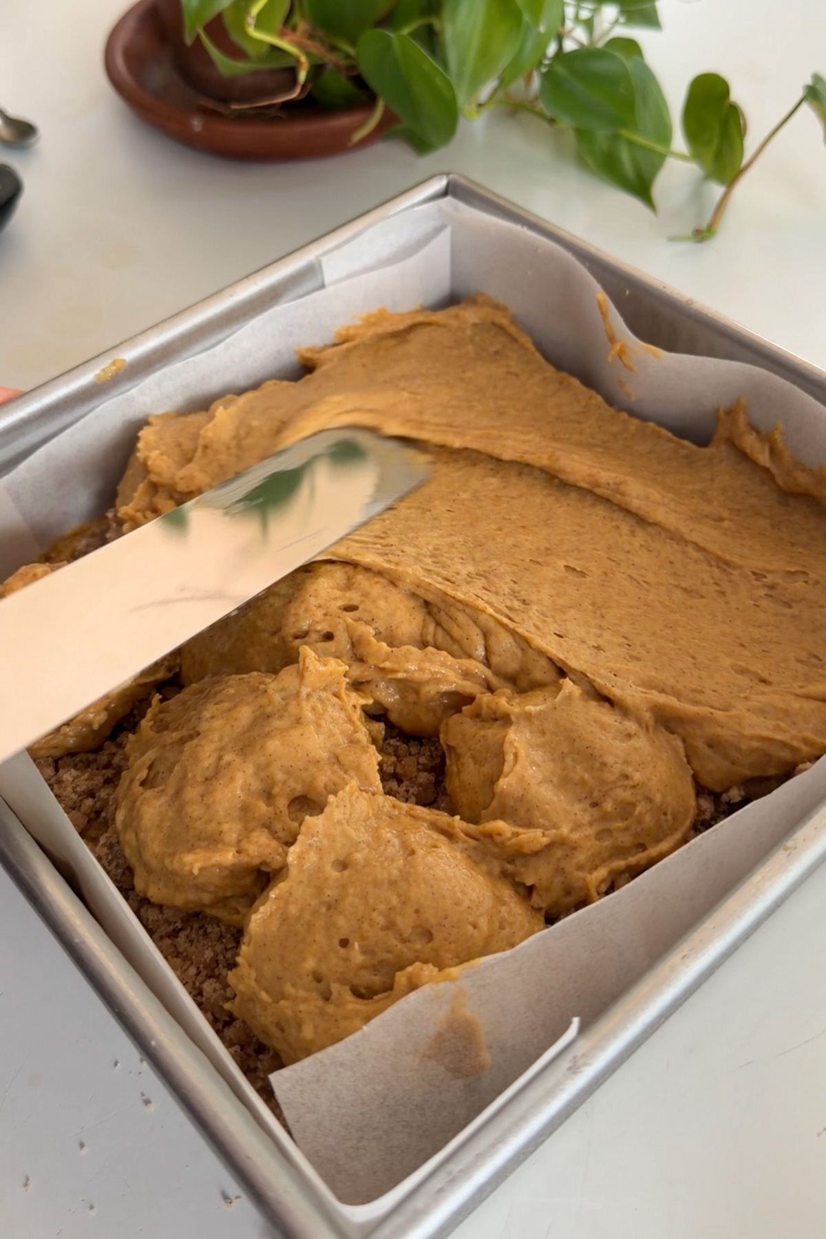A knife smoothing pumpkin coffee cake batter over a layer of streusel.