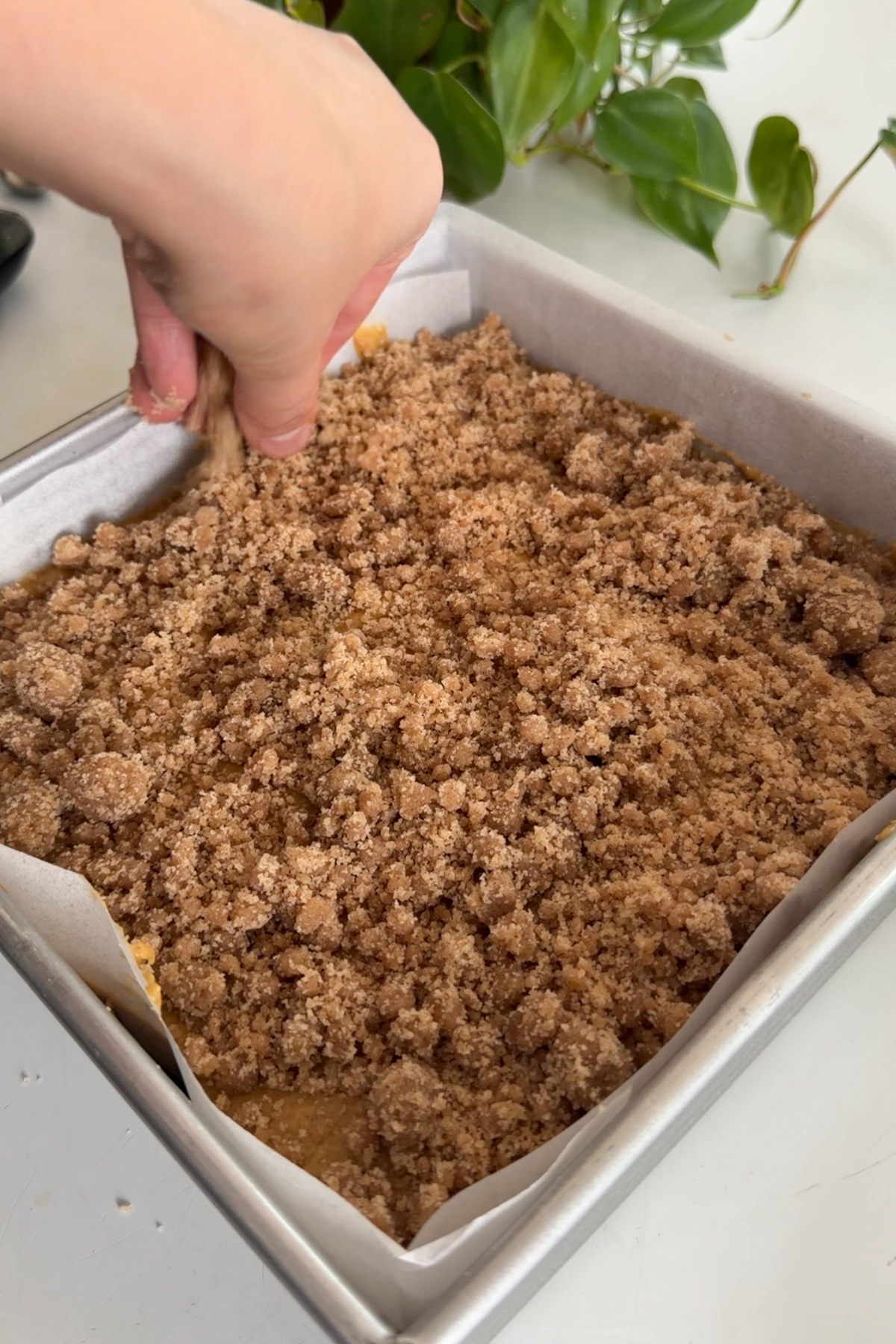 A hand putting streusel on top of a pumpkin coffee cake before baking.