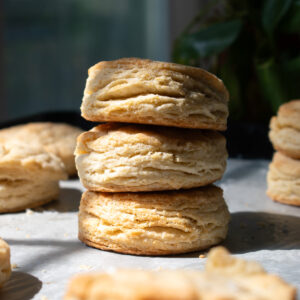 Three golden flaky sourdough discard biscuits stacked on top of each other on a parchment lined baking sheet surrounded by more biscuits.
