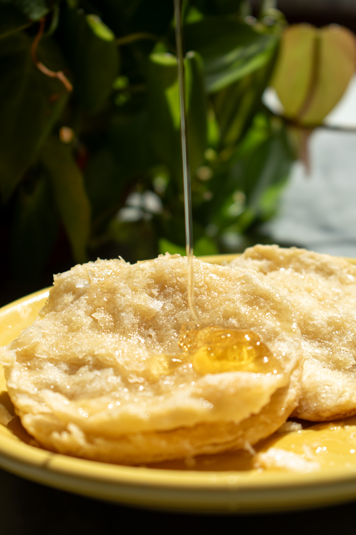 A buttered, flaky biscuit on a yellow plate, with honey pouring over it.