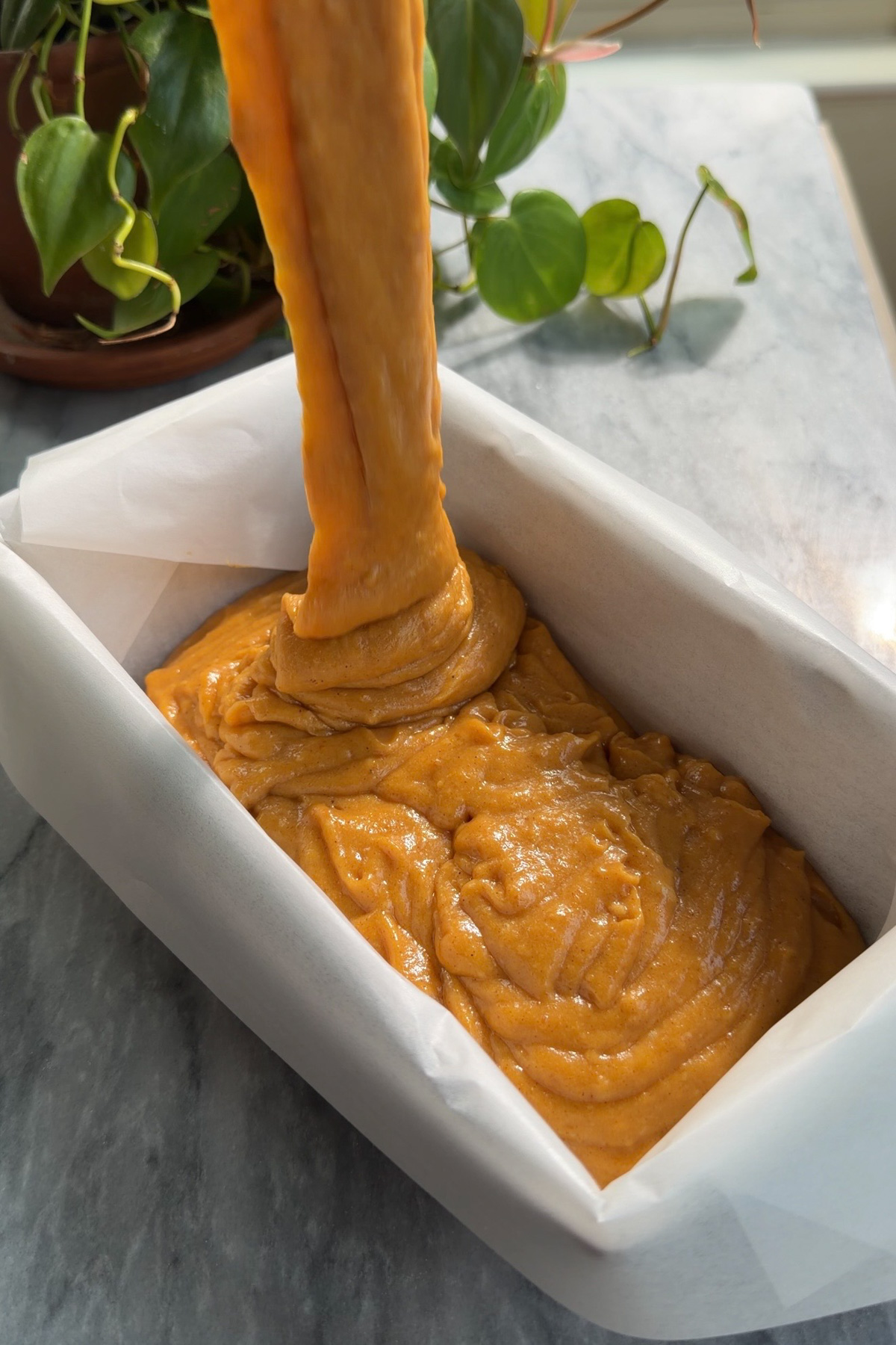 Pumpkin bread batter pouring into a lined 9x5 loaf pan before baking.