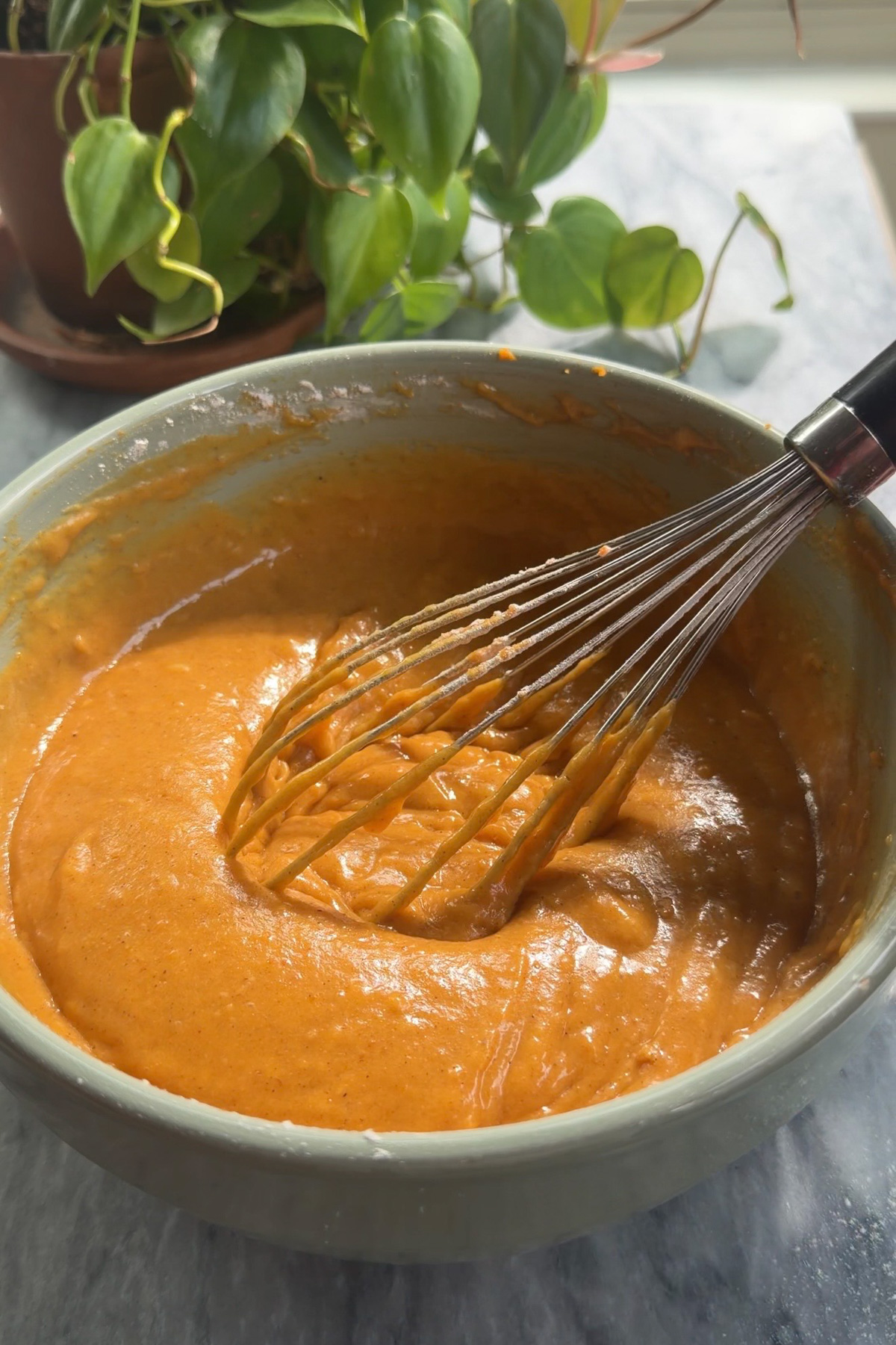 Pumpkin bread batter in a green mixing bowl with a whisk in it.