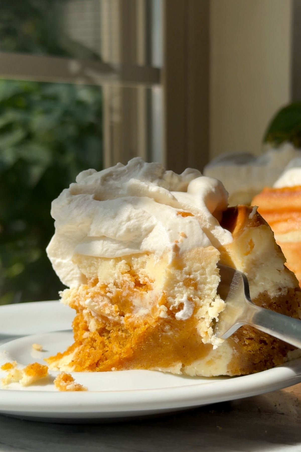 A fork slicing into a piece of pumpkin cake cheesecake with brown sugar whipped cream.