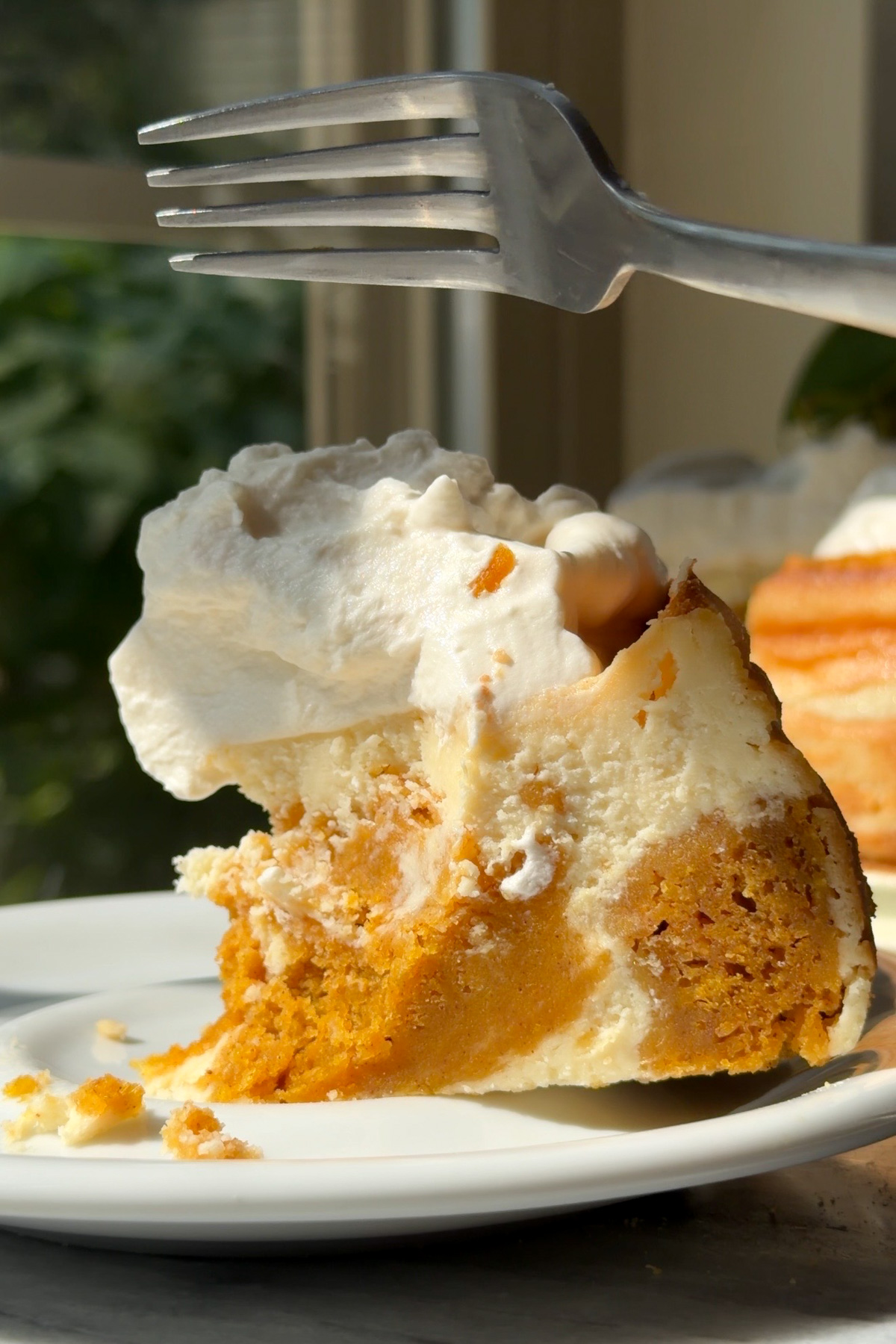 A fork slicing into a piece of pumpkin cake cheesecake with brown sugar whipped cream.