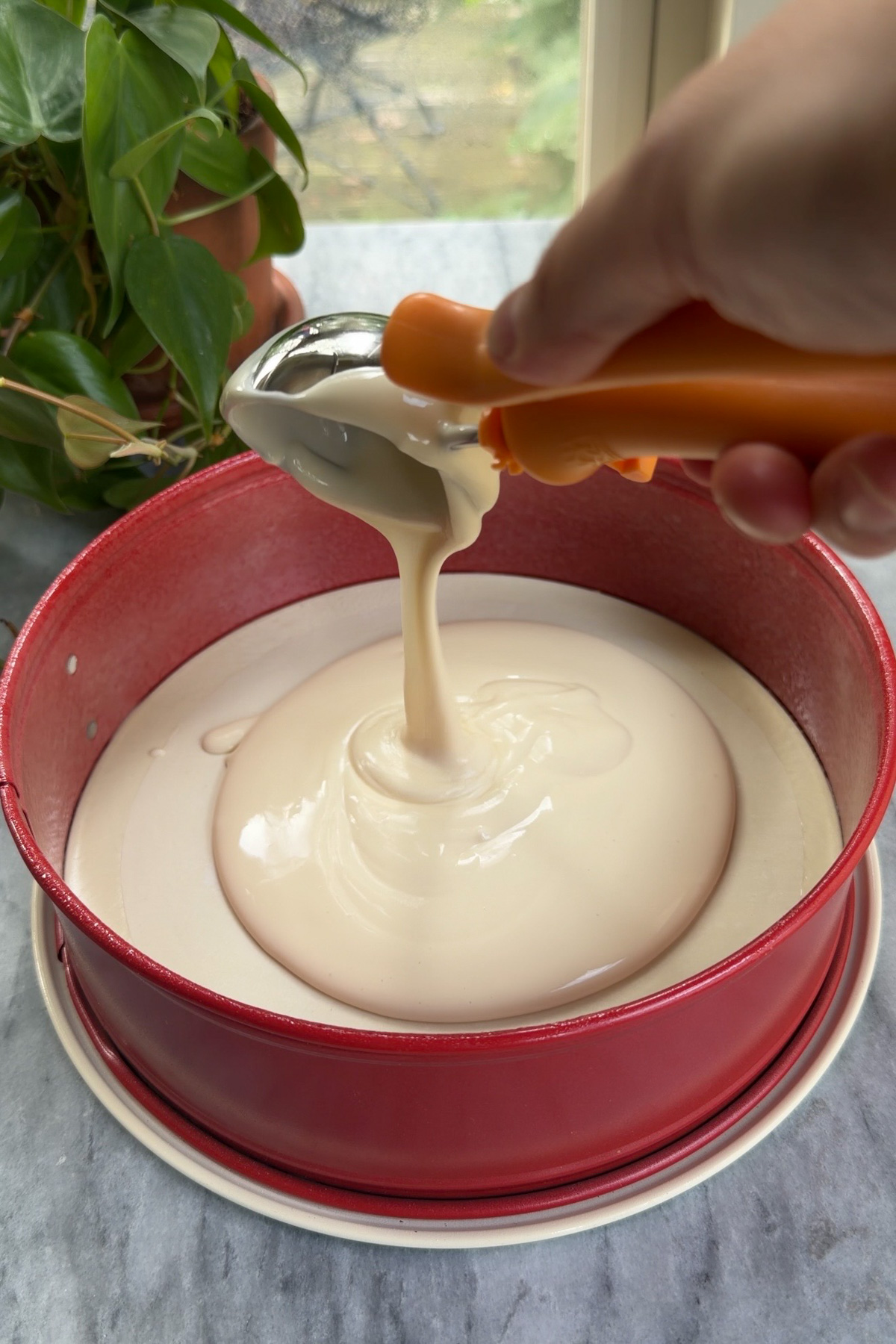 Cheesecake batter being poured into a red springform pan for pumpkin cake cheesecake.