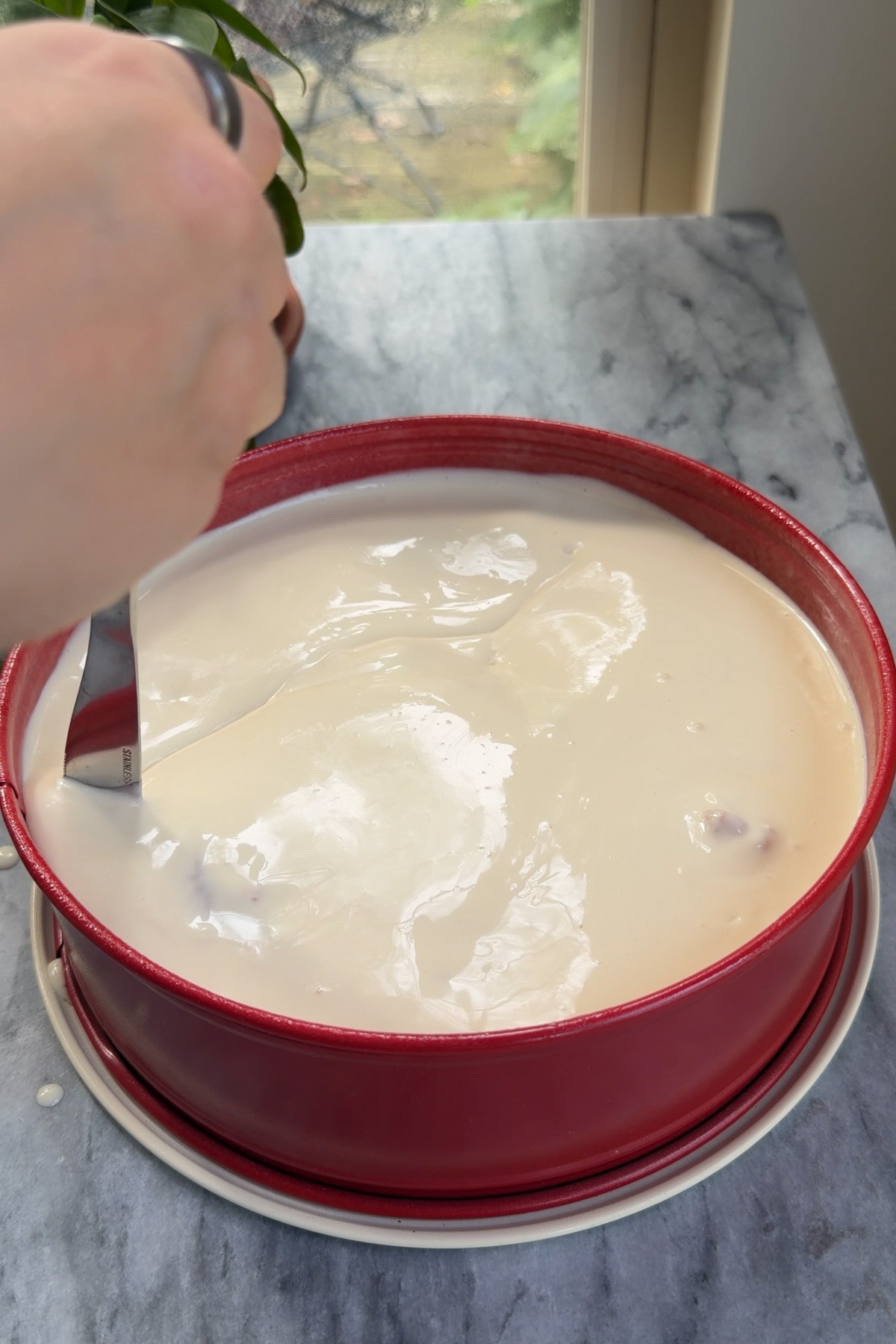 A hand swirling pumpkin cake cheesecake together with a butter knife.