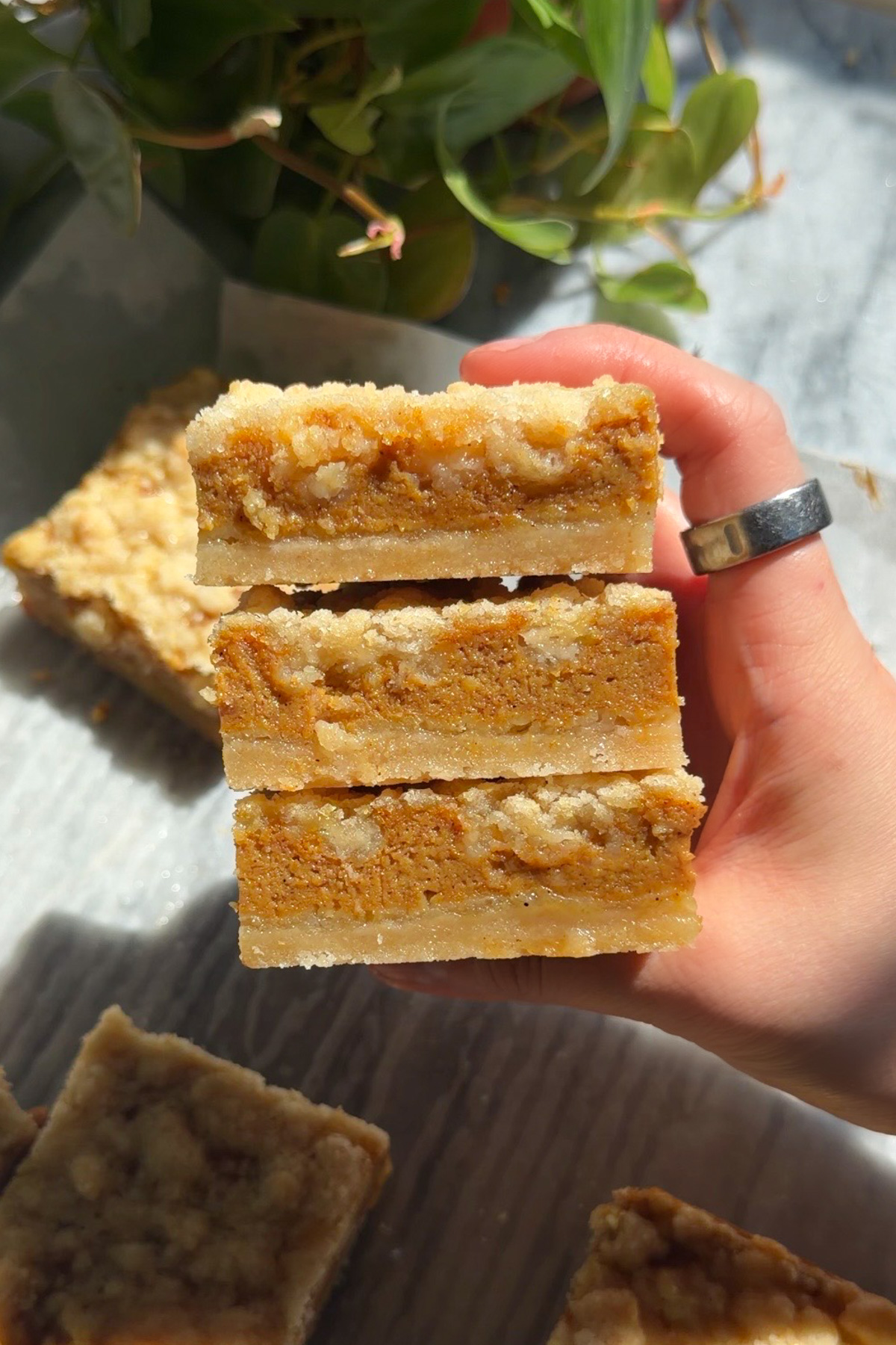 A hand holding three pumpkin pie crumb bars stacked on top of each other.