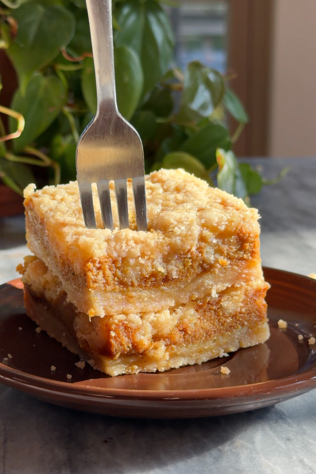 A fork cutting into two stacked pumpkin pie crumb bars on a brown dessert plate.