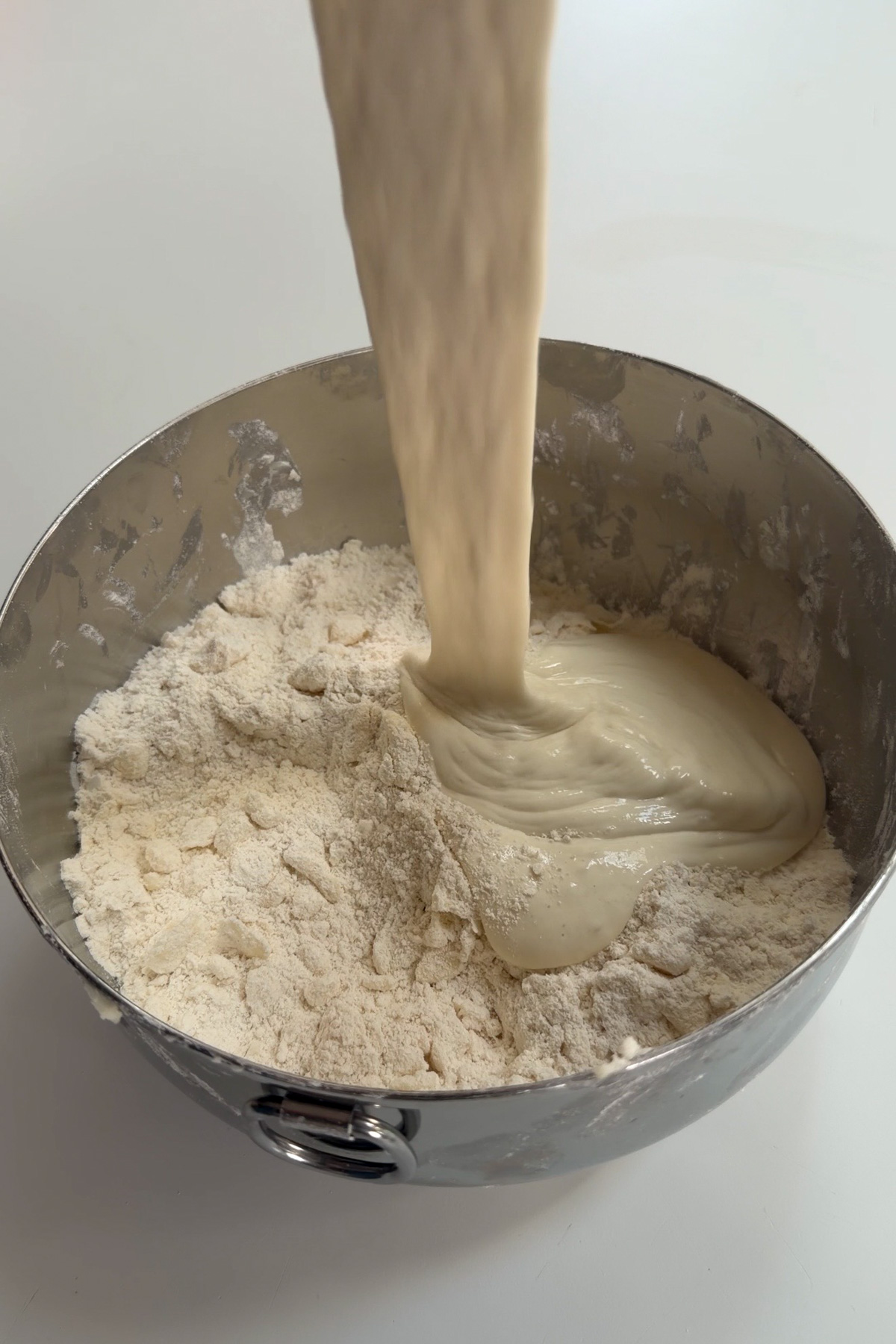 The wet ingredients are being added to the dry ingredients for sourdough discard biscuits in a metal mixing bowl on a white countertop.