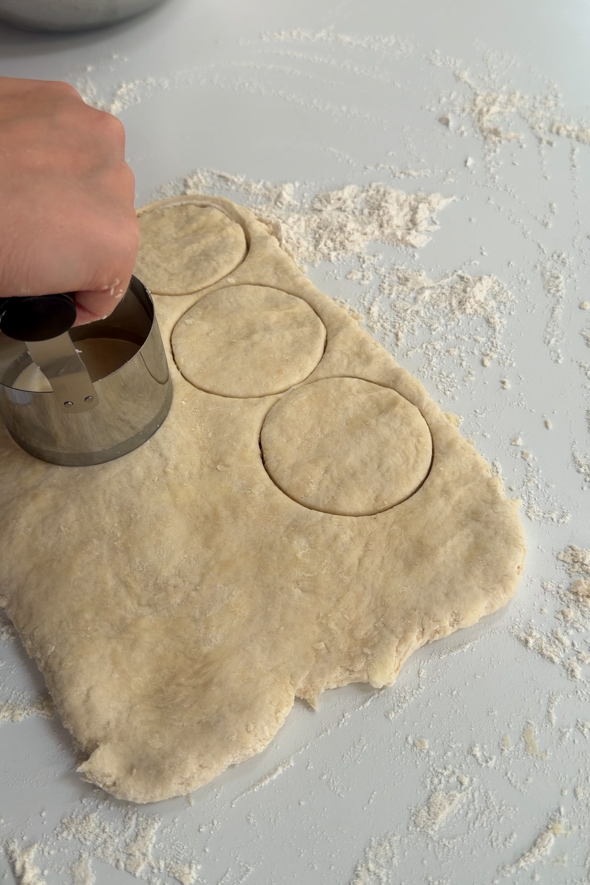 Sourdough discard biscuit dough is being cut into circles on a floured countertop.