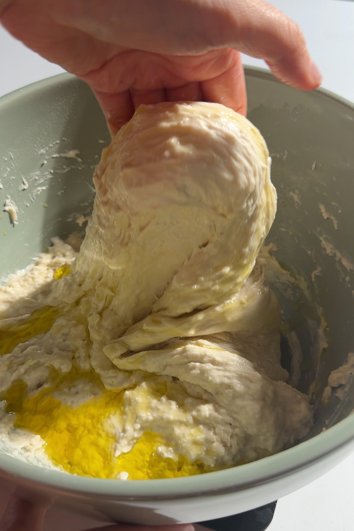A hand stretching and folding sourdough discard focaccia bread dough in a green mixing bowl before shaping.
