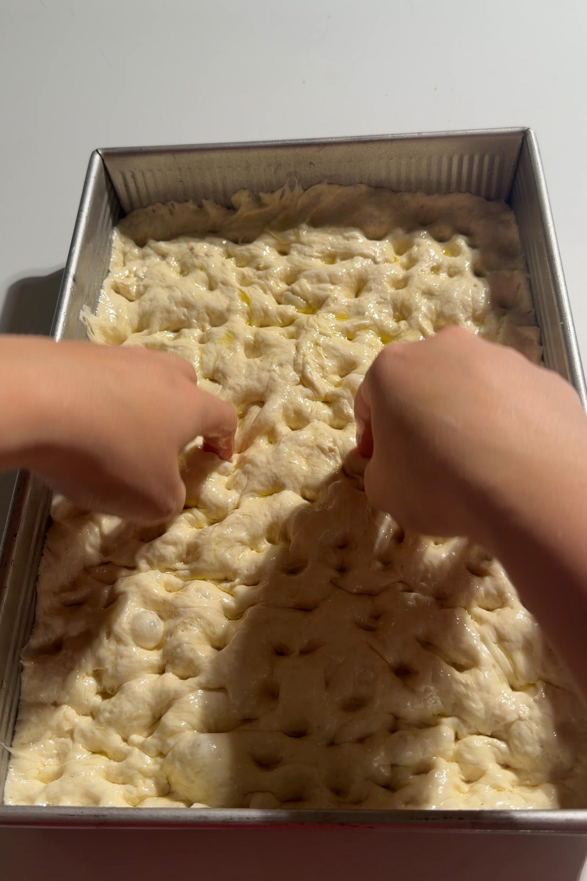 Two hands shaping and dimpling sourdough discard focaccia bread dough in a 9x13 pan after the final proof and before baking.