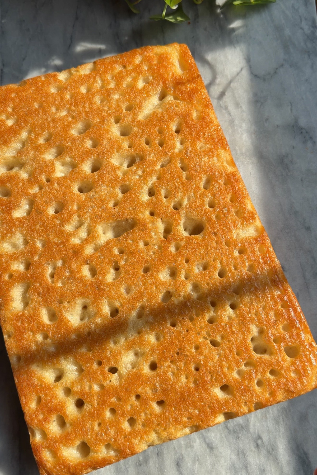 The golden bottom side of sourdough discard focaccia on a marble countertop.