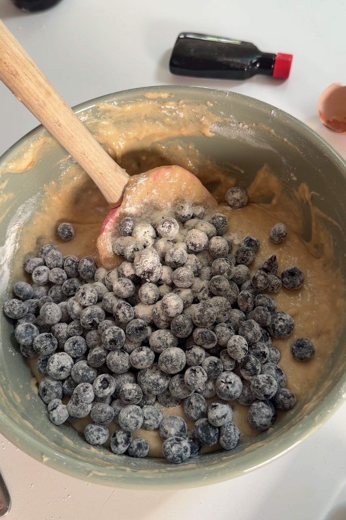 Banana bread muffin batter for blueberry banana muffins in a green mixing bowl with flour-coated blueberries on top before mixing.