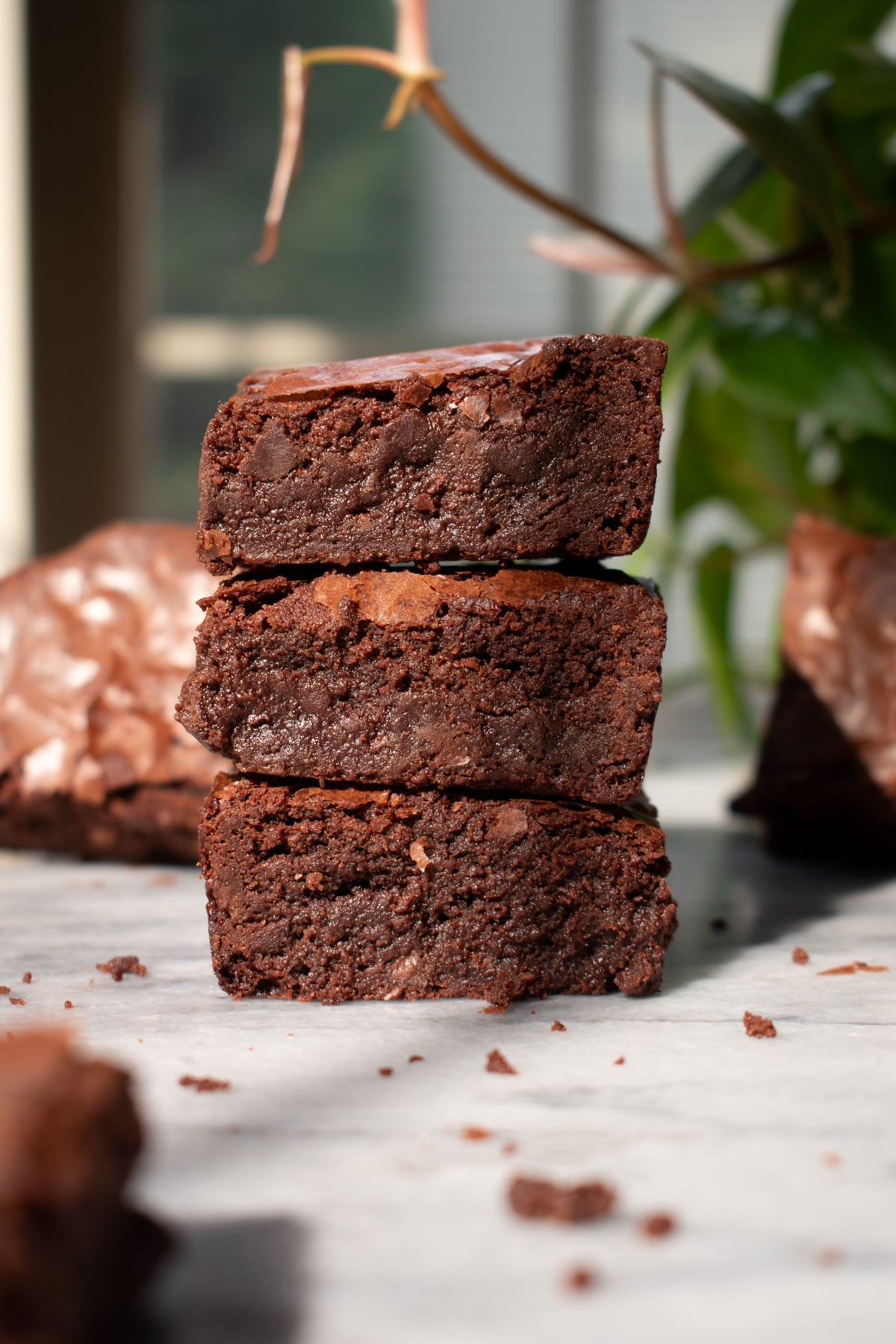 Three crackly fudgy brownies stacked on top of each other on a marble countertop.