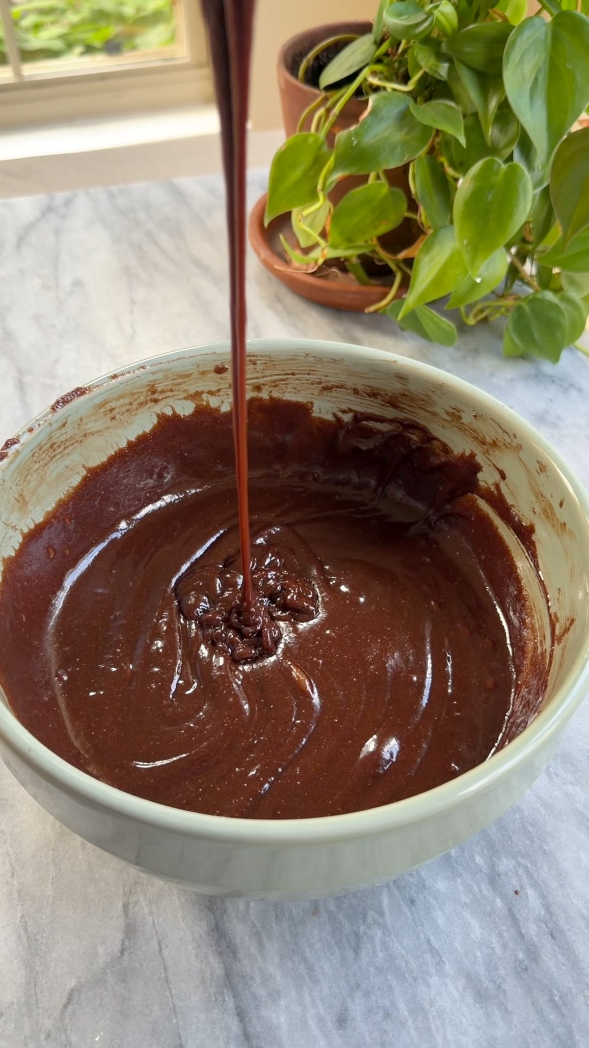 The wet ingredients for brownie batter in a green mixing bowl on a marble countertop.